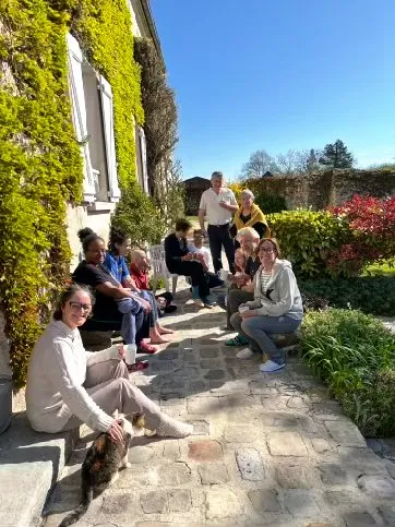 Des stagiaires assis au soleil sur les marches d’une maison aux murs couverts de vigne vierge.