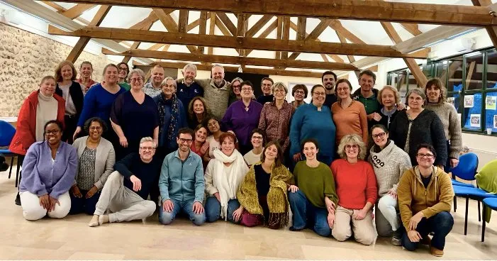 Une quarantaine de stagiaires souriants posent ensemble dans une salle à la charpente apparente.
