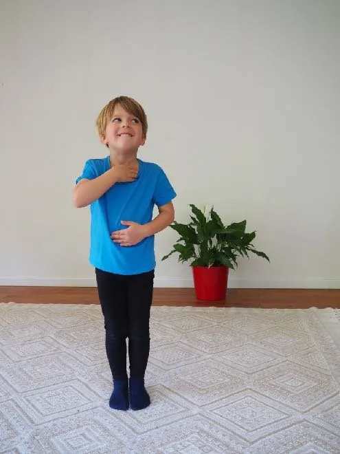 Un jeune garçon debout, une main posée sur la poitrine et l’autre sur le ventre.