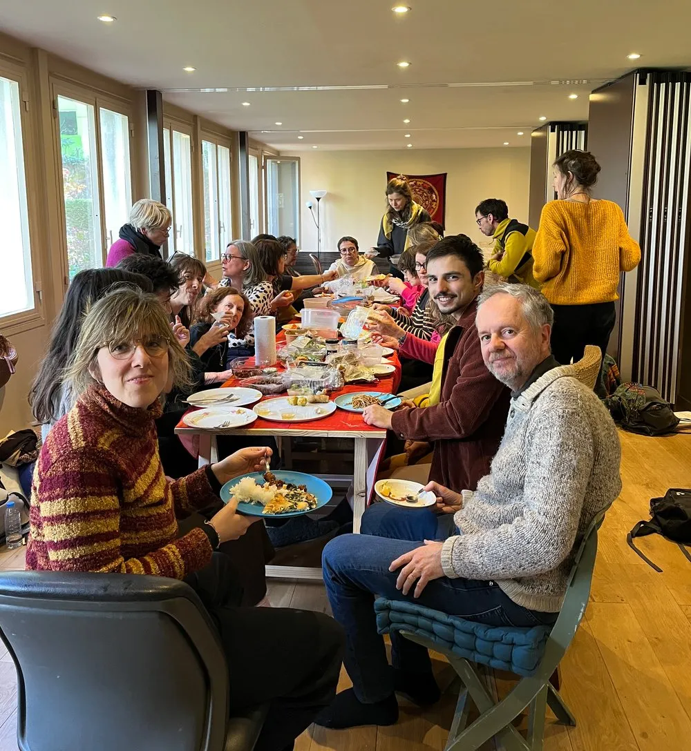 Une longue tablée de participants partageant un repas dans une salle lumineuse