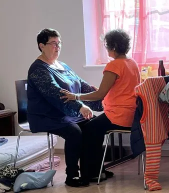 Une praticienne accompagne une femme assise en posant les mains sur ses bras.